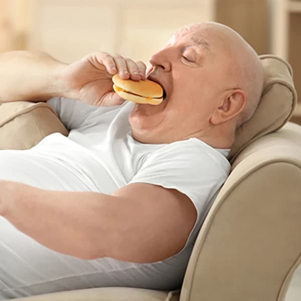 Fat senior man watching TV and eating hamburger